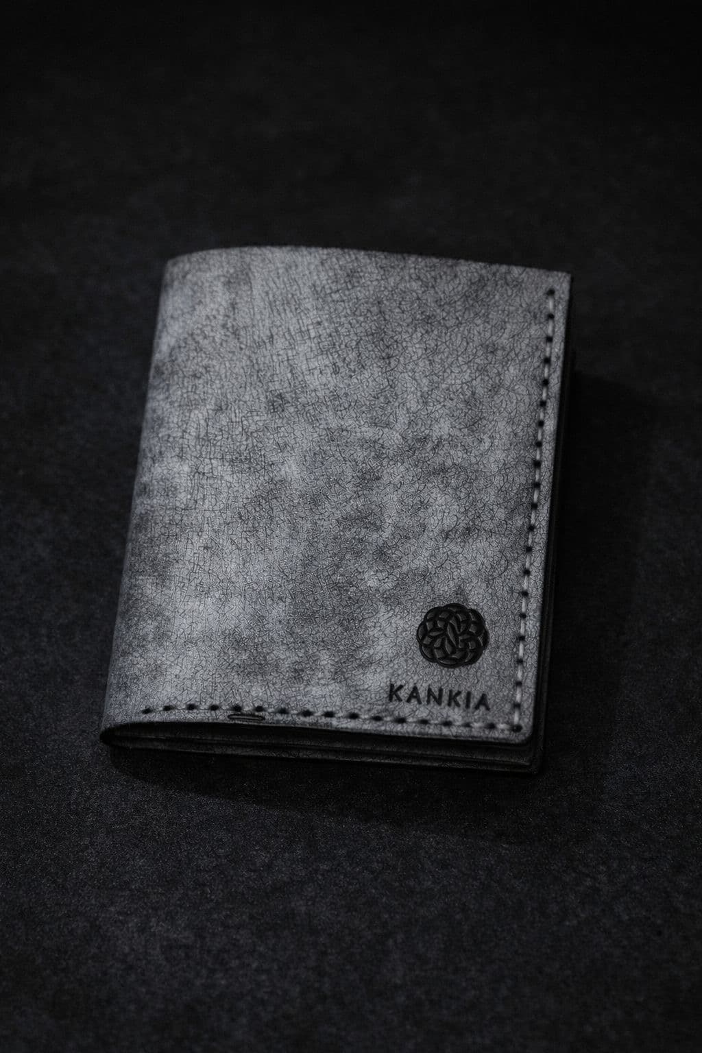 Kankia grey crackle-leather bifold wallet, closed — Kankia logo stamped in black, dark studio